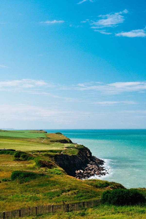 vertical-shot-of-cliff-with-a-grassy-field-near-the-sea-under-a-blue-sky-at-daytime-in-france