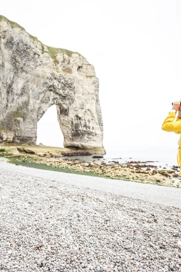 young-female-tourist-in-yellow-raincoat-visiting-famous-coastline-with-high-cliffs-in-etretat-in-france